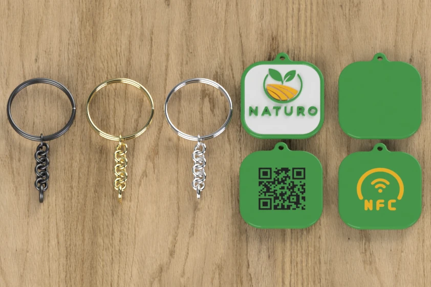 Kwadratowe smart breloki z logo Naturo, kodem QR i symbolem NFC, obok kółka i łańcuszki w trzech kolorach